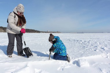 Kadın, çocuğa eskimo evi yapmak için kar kesmeyi öğretiyor.