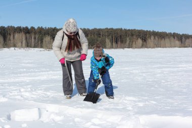 Bir kadın bir çocuğa eskimo evi yapmak için kar bloğu kazmayı öğretiyor.