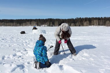 Kadın, çocuğa eskimo evi yapmak için kar kesmeyi öğretiyor.