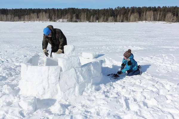 Homme adulte et petit garçon construisant un igloo sur une clairière enneigée — Photo