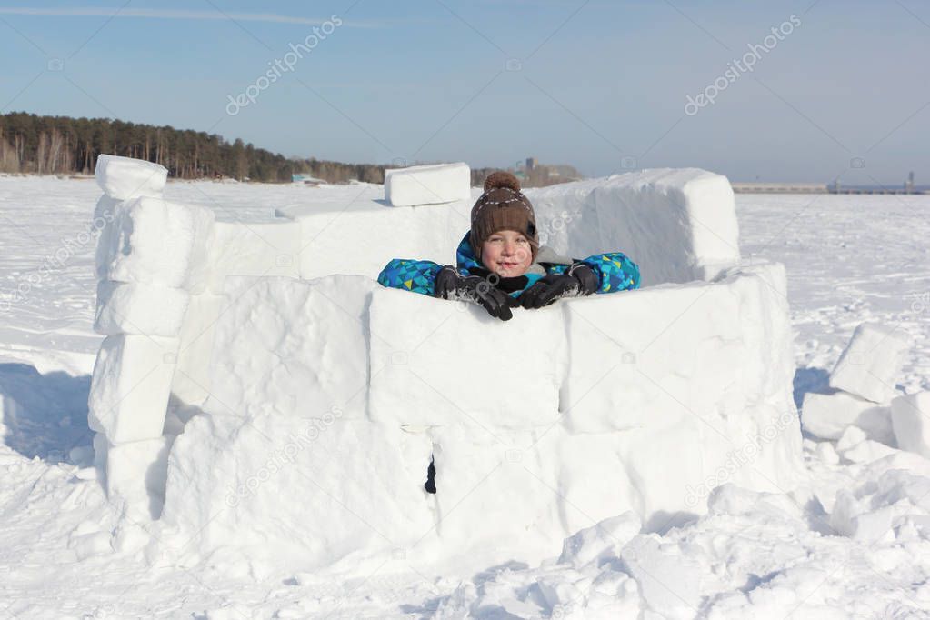 Happy cheerful boy sitting in an unfinished igloo 