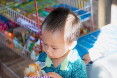Küçük bir çocuğun bakkalda bir dilim ekmeğin tadını çıkarırken. İki yaşındaki Asyalı çocuk..