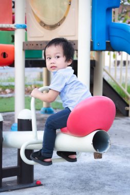 Dışarıda bir parkta tahterevalliyle oynayan sevimli bir çocuğun dikey çekimi. Küçük şirin bir Asyalı çocuğun kameraya bakışının arkası. 2-3 yaşındaki oğlu..