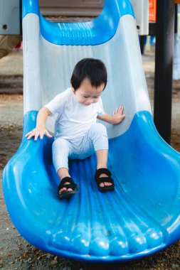 2-3 yıl mutlu küçük bir çocuk, açık hava oyun parkında kaydırağında oynarken gülümsüyor. Dikey görüntü. Okul öncesi çocuk teneffüsünde oynar ya da oyun parkına park eder.