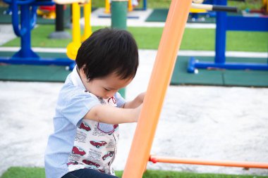 Küçük Asyalı çocuk turuncu tırmanma duvarına tırmanıyor. Şirin 2-3 yaşındaki bir çocuk yaz ya da bahar aylarında açık hava çocuk parkında tırmanmak için can atıyor. Oyun ve egzersiz konsepti.