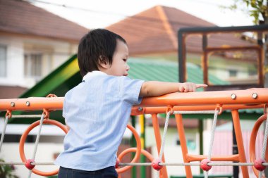Küçük çocuk dışarıda oyun oynarken eğleniyor. 2-3 yaşlarında Asyalı bir çocuk tek eliyle Orman Spor Salonu 'na tırmanıyor. Oyun oynayan çocuklar için güvenlik kavramı.