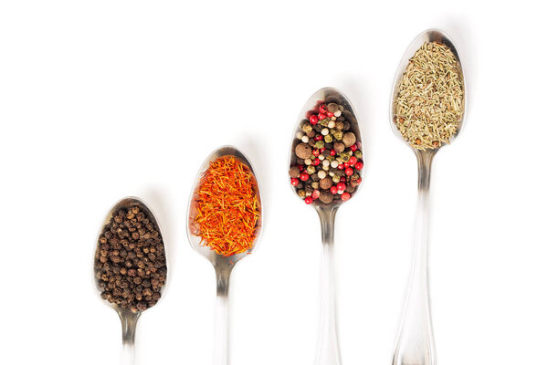 Different spices in iron spoons isolated on white background. View from the top of dried rosemary, saffron, pepper. 