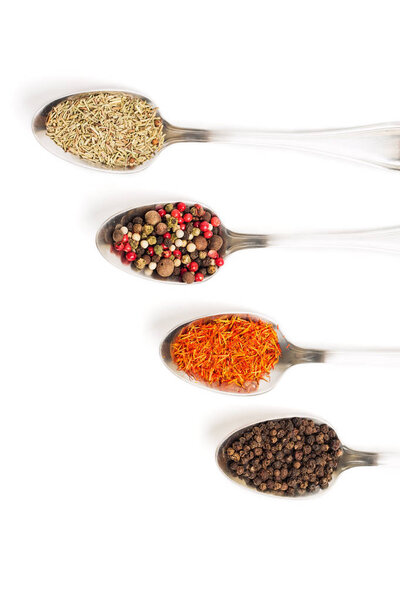 Different spices in iron spoons isolated on white background. View from the top of dried rosemary, saffron, pepper. 