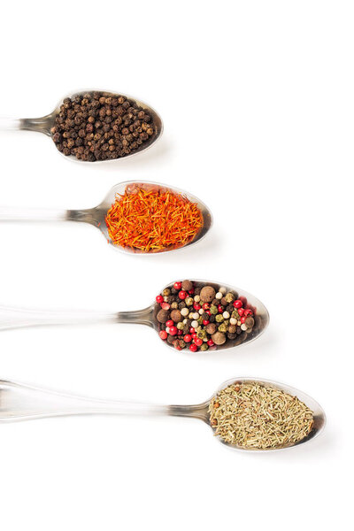Different spices in iron spoons isolated on white background. View from the top of dried rosemary, saffron, pepper. 