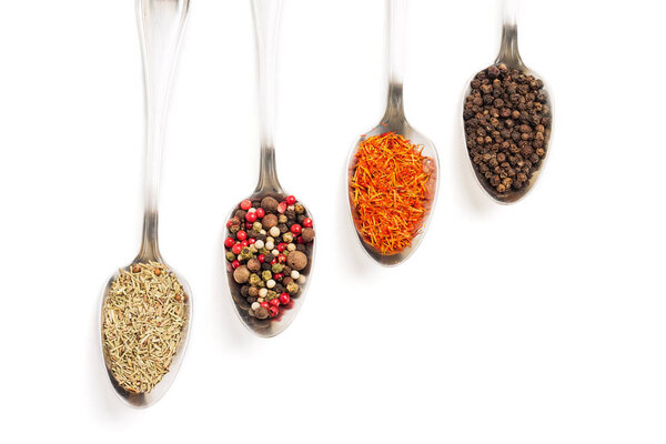 Different spices in iron spoons isolated on white background. View from the top of dried rosemary, saffron, pepper. 