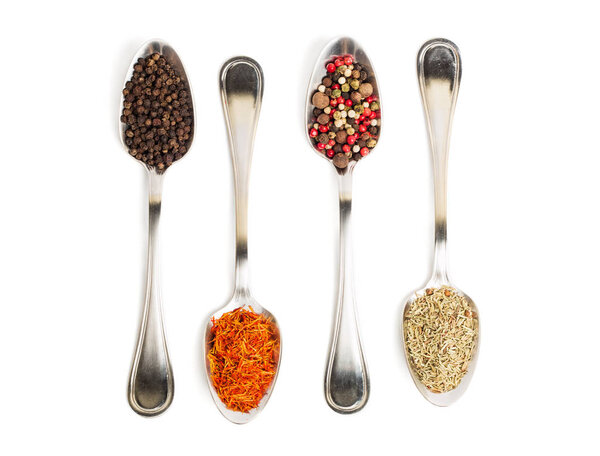 Different spices in iron spoons isolated on white background. View from the top of dried rosemary, saffron, pepper. 