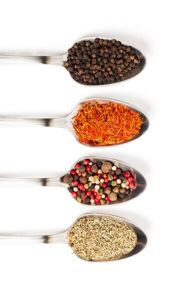 Different spices in iron spoons isolated on white background. View from the top of dried rosemary, saffron, pepper. 