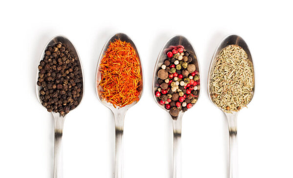 Different spices in iron spoons isolated on white background. View from the top of dried rosemary, saffron, pepper. 