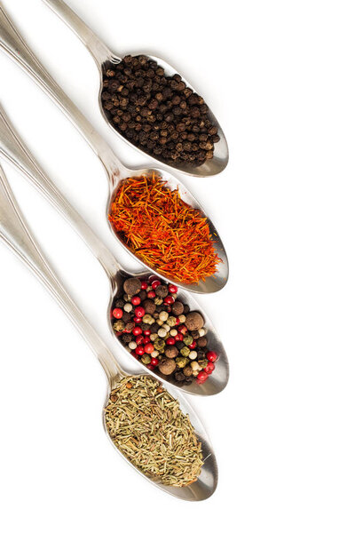 Different spices in iron spoons isolated on white background. View from the top of dried rosemary, saffron, pepper. 