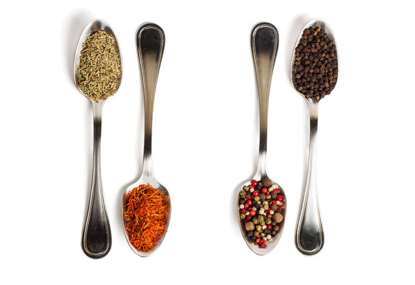 Different spices in iron spoons isolated on white background. View from the top of dried rosemary, saffron, pepper. 