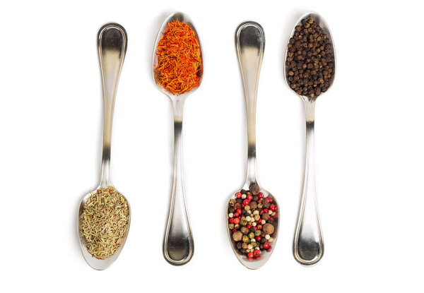 Different spices in iron spoons isolated on white background. View from the top of dried rosemary, saffron, pepper. 