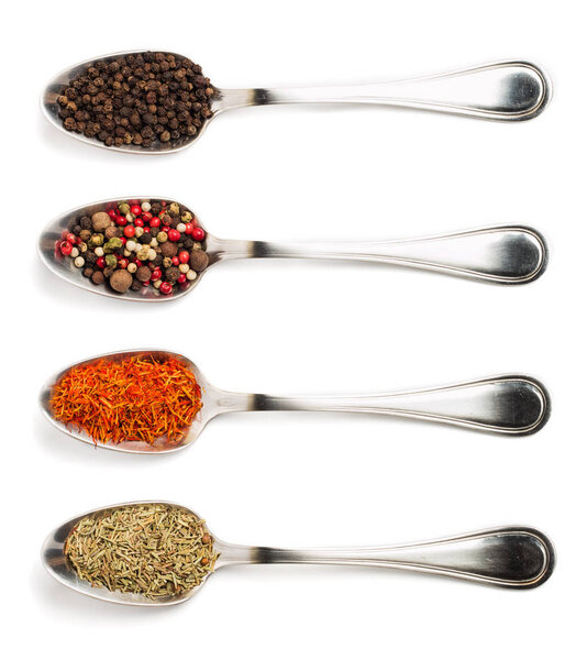 Different spices in iron spoons isolated on white background. View from the top of dried rosemary, saffron, pepper. 