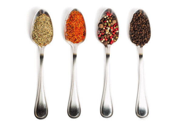 Different spices in iron spoons isolated on white background. View from the top of dried rosemary, saffron, pepper. 
