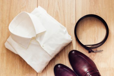 Düz klasik erkek giyim kahverengi ayakkabı, kemer ve beyaz gömlek gibi ahşap arka plan üzerinde set yatıyordu. Üstten görünüm.