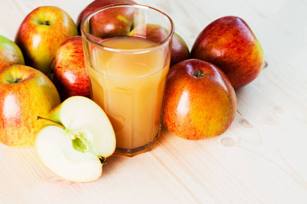 Glass of fresh apple cider and half apple near autumn apples. Wooden background, space for text. Autumnal background.