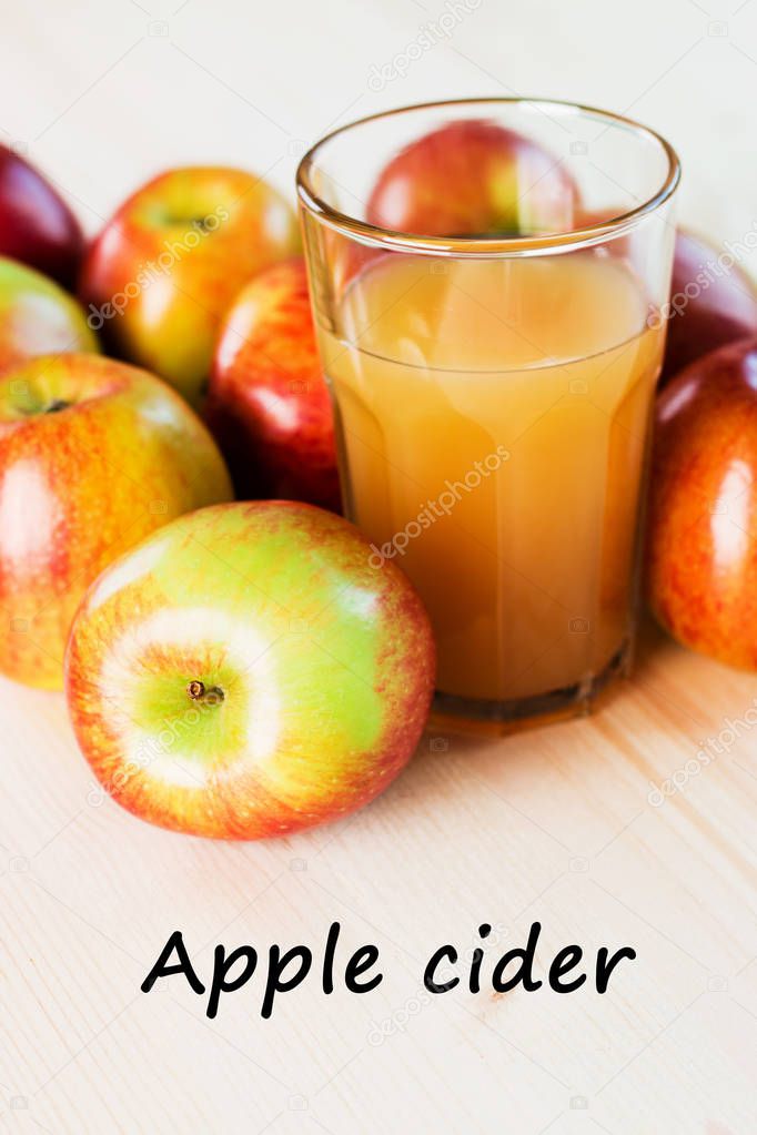Glass of fresh apple cider near autumn apples. Wooden background, text apple cider.