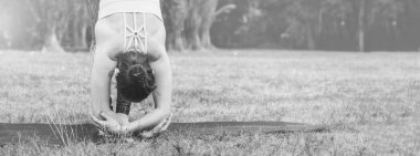 Pratik yoga Uttanasana yoga poz içinde ayakta doğada ince genç kadın. Yeşil arka plan, derin germe. İyi sağlıklı ve spor kavram. Metin için yer kopyalayın. Siyah ve beyaz fotoğraf.