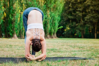 Pratik yoga Uttanasana yoga poz içinde ayakta doğada ince genç kadın. Yeşil arka plan, derin germe. İyi sağlıklı ve spor kavramı. 