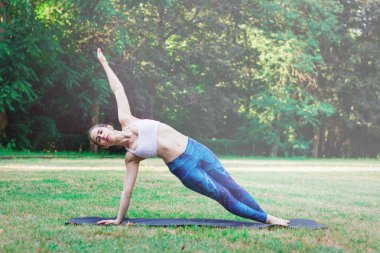 İnce kadın doğada - yan tahta poz, Vasisthasana egzersiz Yoga uygulamak. Mat yeşil zemin üzerine Dengeleme erkek. Sağlıklı ve spor kavram. Tonda etkisi ile yeşil arka plan