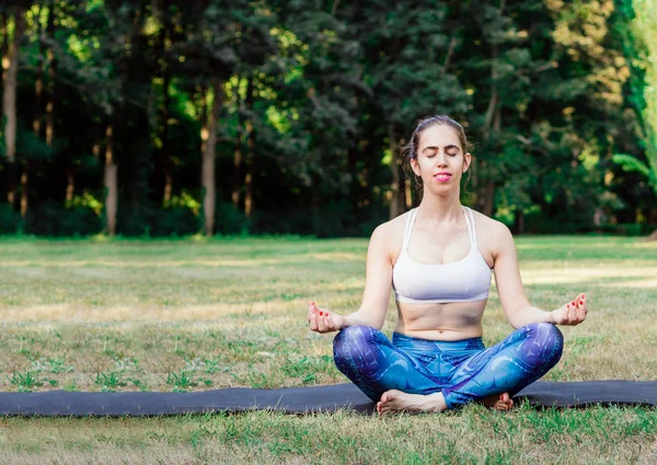 Young woman practicing yoga in nature. Sitting on green grass and meditating.Green background with toned effect. Healthy and sport concept.Copy space for text.