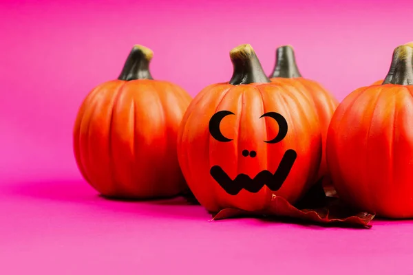 Halloween holiday background. Halloween pumpkin jack o lantern decor with funny faces on pink background. Copy space for text.