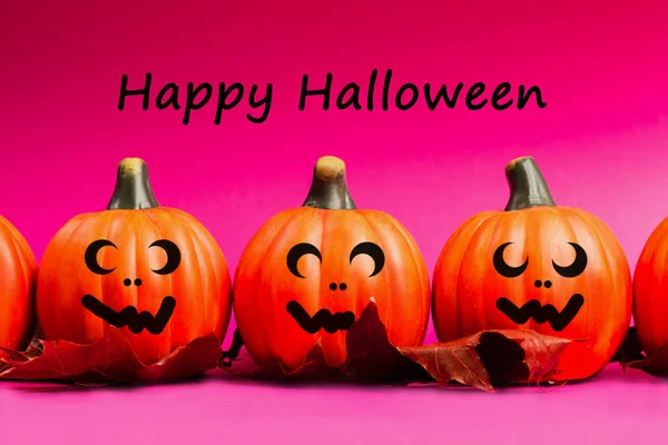 Halloween holiday background. Halloween pumpkin jack o lantern decor with funny faces on pink background. Text happy halloween.