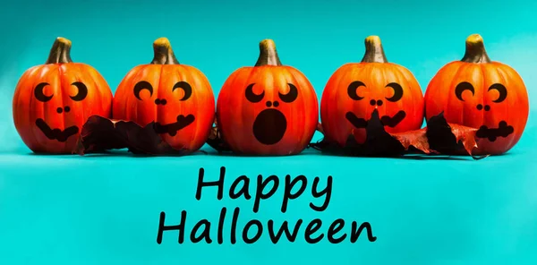 Halloween holiday background. Halloween pumpkin jack o lantern decor with funny faces on blue background. Text happy halloween.