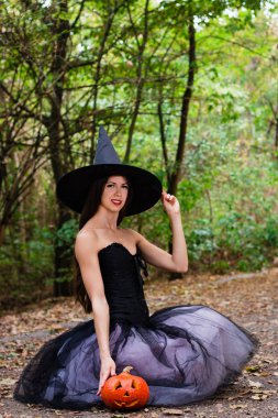 Cadılar Bayramı tatil arka plan. Halloween cadı halloween balkabağı jack o fener dekor ile karanlık bir ormanda komik surat ile. Güzel genç kadın cadı şapka ve kabak tutan kostüm.