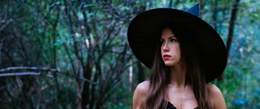 Cadılar Bayramı tatil arka plan. Karanlık bir ormanda halloween cadı. Güzel genç kadın cadı şapka ve kostüm.