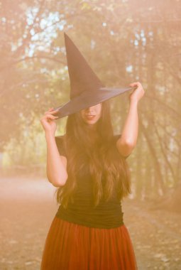 Cadılar Bayramı tatil arka plan. Karanlık bir ormanda halloween cadı. Güzel genç kadın cadı şapka ve turuncu duman arka plan üzerinde kostüm.