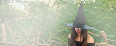 Cadılar Bayramı tatil arka plan. Halloween cadı tonda etkisi ile karanlık bir ormanda. Güzel genç kadın cadı şapka ve kostüm.