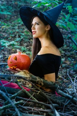 Cadılar Bayramı tatil arka plan. Halloween cadı halloween balkabağı jack o fener dekor ile karanlık bir ormanda komik surat ile. Güzel genç kadın cadı şapka ve kabak tutan kostüm.