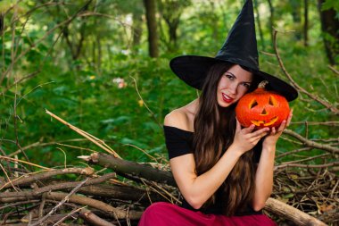 Cadılar Bayramı tatil arka plan. Halloween cadı halloween balkabağı jack o fener dekor ile karanlık bir ormanda komik surat ile. Güzel genç kadın cadı şapka ve kabak tutan kostüm.