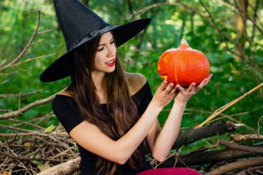 Cadılar Bayramı tatil arka plan. Halloween cadı halloween balkabağı jack o fener dekor ile karanlık bir ormanda komik surat ile. Güzel genç kadın cadı şapka ve kabak tutan kostüm.