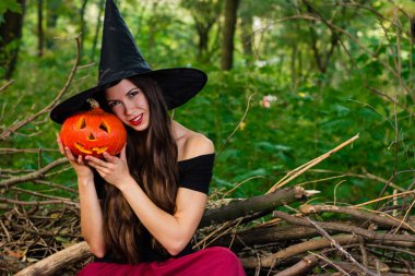 Cadılar Bayramı tatil arka plan. Halloween cadı halloween balkabağı jack o fener dekor ile karanlık bir ormanda komik surat ile. Güzel genç kadın cadı şapka ve kabak tutan kostüm.