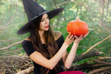 Cadılar Bayramı tatil arka plan. Bir halloween kabak jack o tonda etkisi ile karanlık bir ormanda komik surat ile fener dekor ile halloween cadı. Güzel genç kadın cadı şapka ve kabak tutan kostüm.