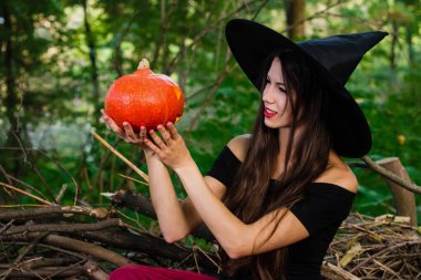 Cadılar Bayramı tatil arka plan. Halloween cadı halloween balkabağı jack o fener dekor ile karanlık bir ormanda komik surat ile. Güzel genç kadın cadı şapka ve kabak tutan kostüm.
