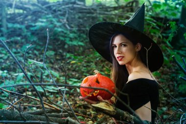 Cadılar Bayramı tatil arka plan. Halloween cadı halloween balkabağı jack o fener dekor ile karanlık bir ormanda komik surat ile. Güzel genç kadın cadı şapka ve kabak tutan kostüm.