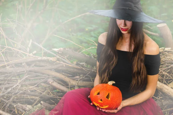 ハロウィーンの休日背景 ハロウィン魔女トーン効果と暗い森で変な顔とハロウィーン カボチャのジャック ランタン装飾が施されました 魔女帽子と衣装の美しい若い女性 — ストック写真