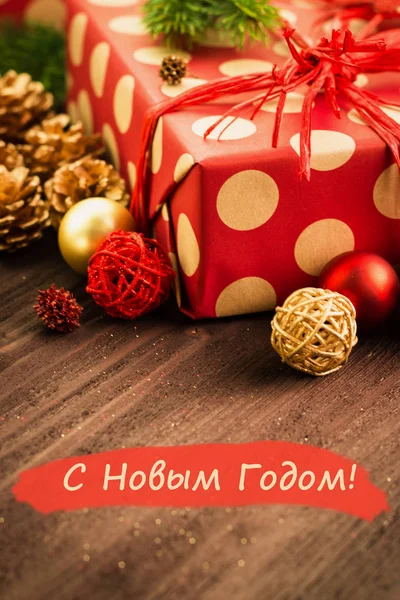 クリスマスとお正月のお祭りの装飾は ゴールデン ボールとゴールデン Fir コーン提示に包まれた赤い紙赤に新年あけましておめでとうございます でロシア新年あけましておめでとうございます のテキストで茶色の木製の背景に金色の円 — ストック写真