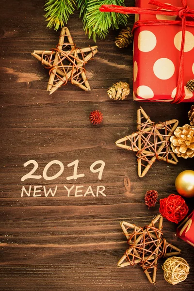 Christmas and New Year\'s Day festive decoration, red and golden balls, fir cones, branches and wooden stars with present wrapped in red paper with golden circles on brown wood background with text 2019 New Year. Flat lay. View from above.