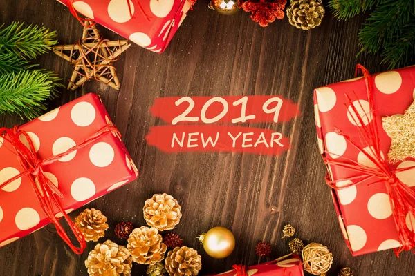 Christmas and New Year\'s Day festive decoration, red and golden balls, fir cones, branches and wooden stars with presents wrapped in red paper with golden circles on brown wood background with text 2019 New Year on red. Flat lay. View from above.