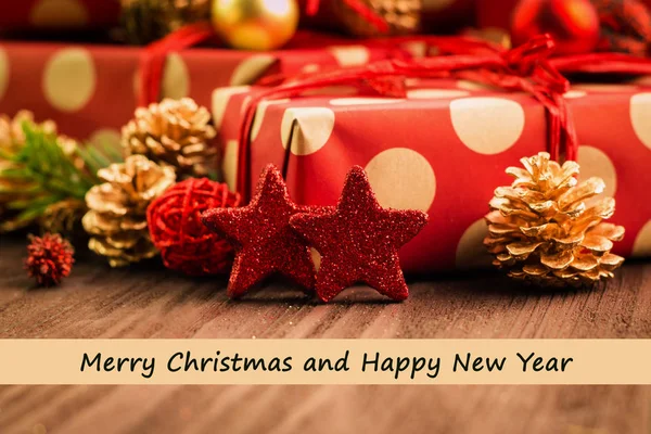 Christmas and New Year's Day festive decoration, red and golden balls, multicolored fir cones and branches, red stars with presents wrapped in red paper with golden circles on brown wood background with text Merry Christmas and Happy new year on beig