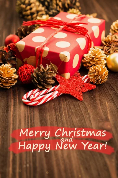 Christmas and New Year's Day decoration, balls, fir cones, candies and stars with present wrapped in red paper with golden circles on wood background with text Merry Christmas and Happy New Year.