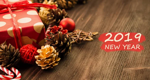 New Year\'s Day decoration, balls, fir cones, candies and stars with present wrapped in red paper with golden circles on wood background with text 2019 New Year.